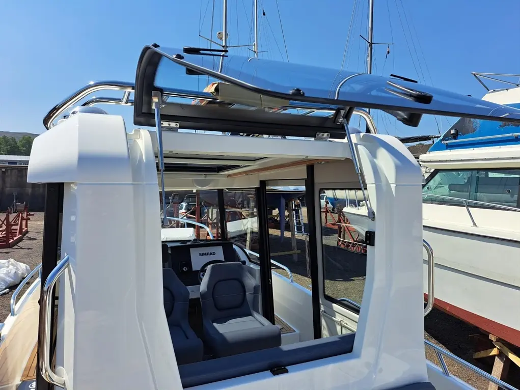 Interior view of a modern boat featuring two gray seats, a SIMRAD dashboard, and a retractable hardtop in a marina.